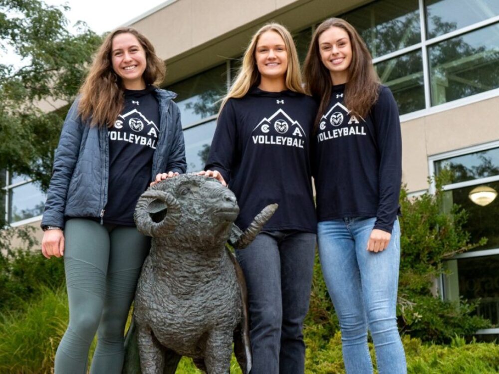 Volleyball players Alyssa, Jacqi and Karina stand with the Moby Ram statue