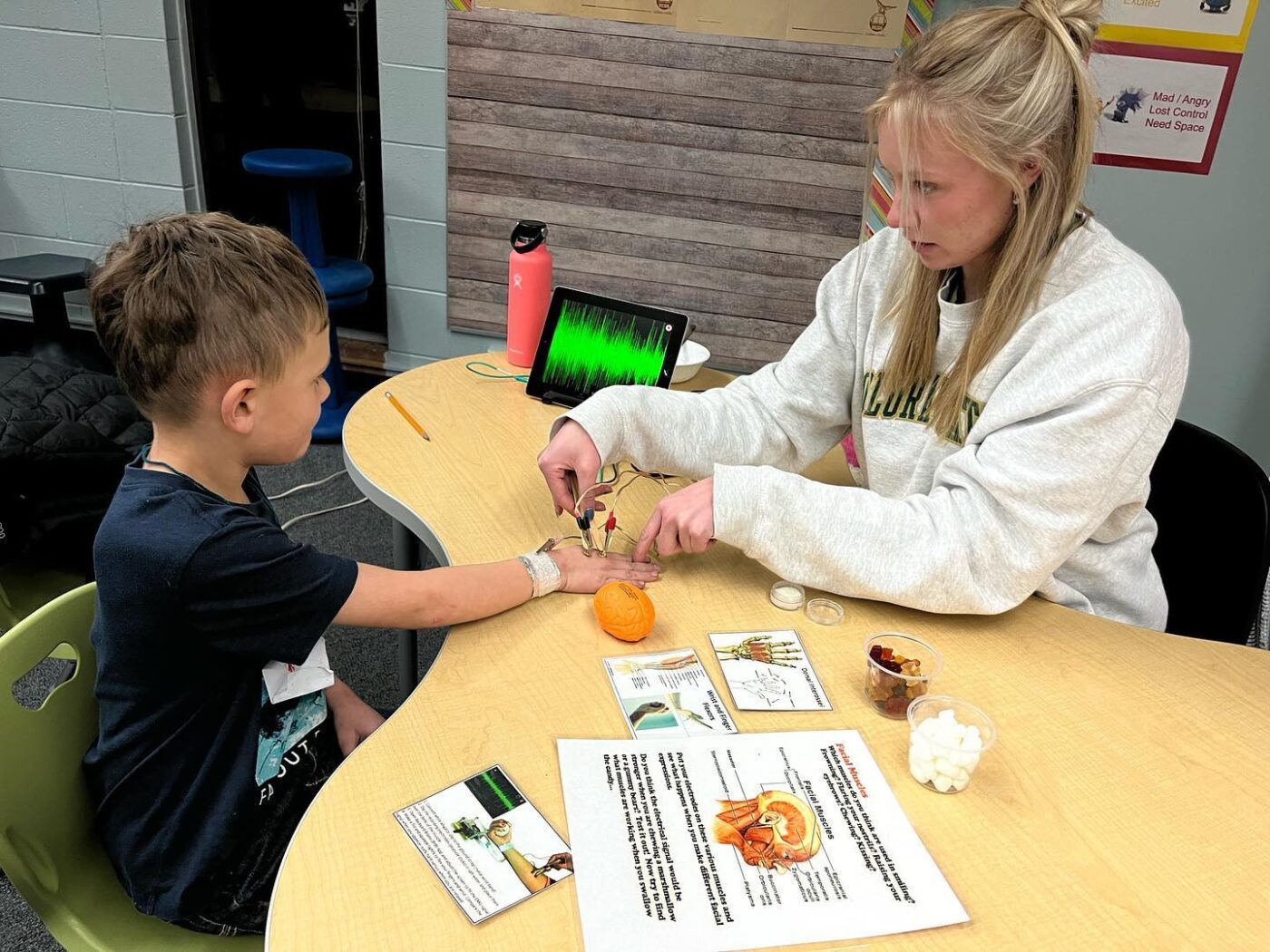 Student sitting with a elementary school child while they perform an experiment