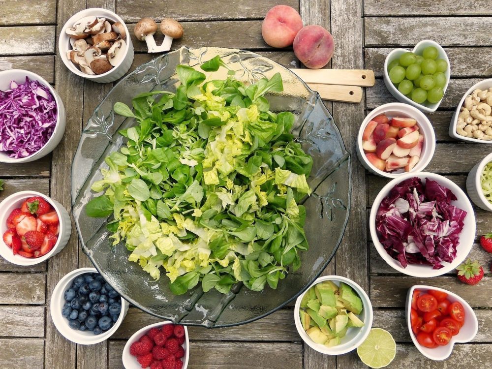 small bowls of fruits and vegetables surrounding large bowl of chopped lettuce