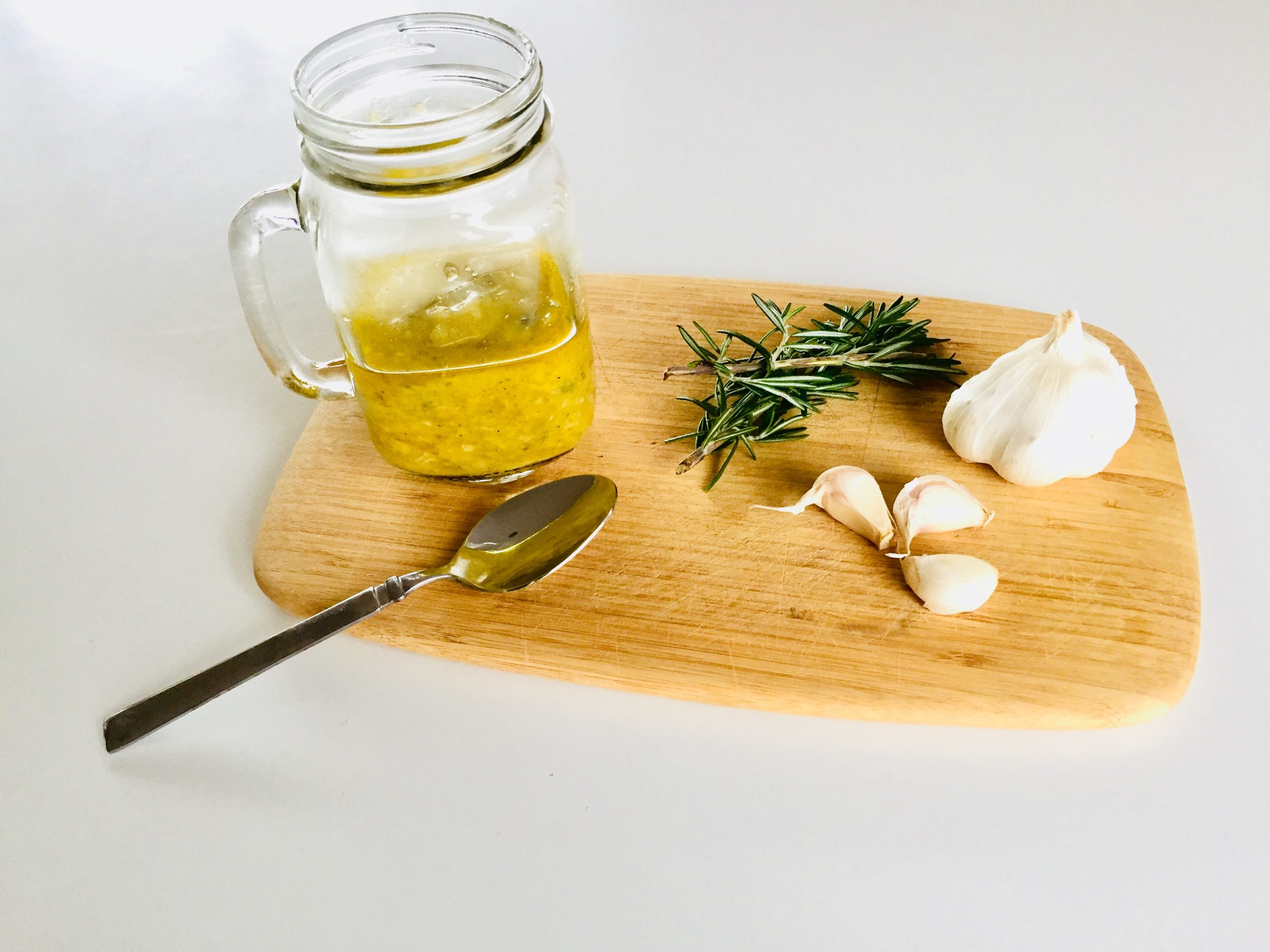 roasted garlic dressing in jar with a spoon, fresh garlic cloves on a cutting board