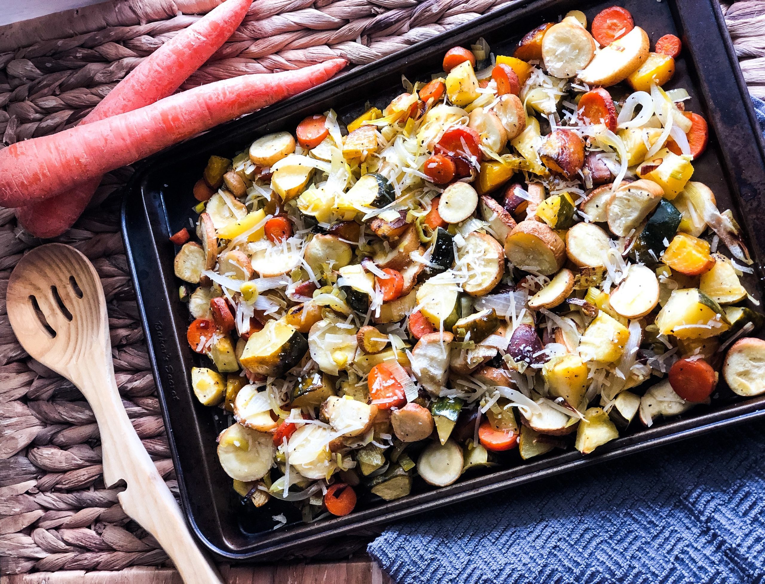 Roasted vegetables on a sheet pan with whole carrots and wooden spoon on the side