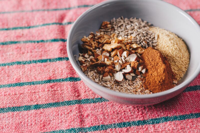 Bowl with chopped almonds, sunflower seeds, oats, cinnamon and other grains.