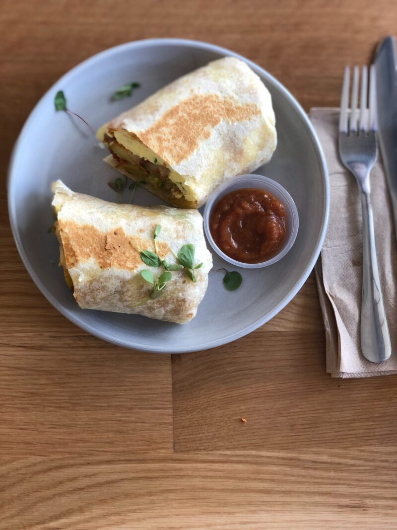 breakfast burrito cut in half, on plate next to silverware