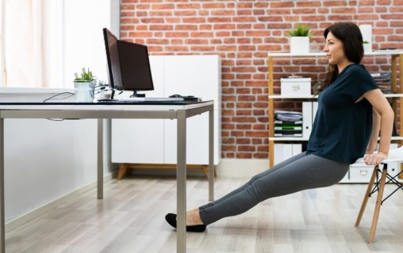 Woman using a chair to do tricep dips at her desk