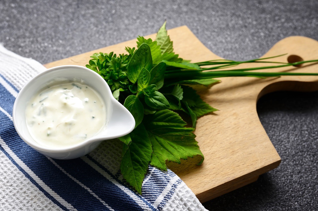 Ranch dressing in a small bowl, with fresh herbs on cutting board
