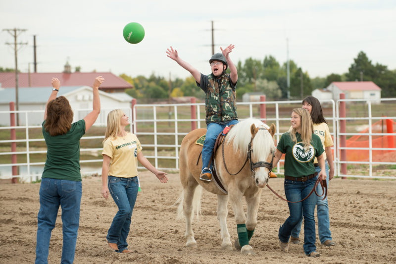 OT students playing catch with a child on a horse in a therapy session