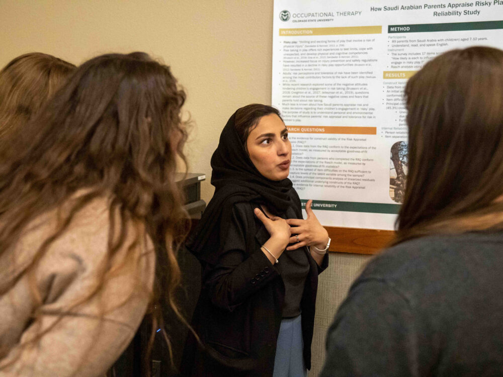 A student explaining her research to a small group with her research poster behind her