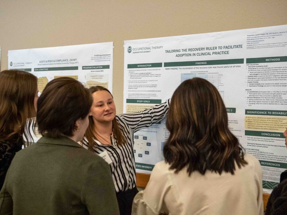 A student explaining her research to multiple other people while motioning toward the research poster