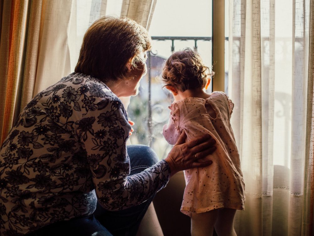 Grandmother and grandchild looking outside window.