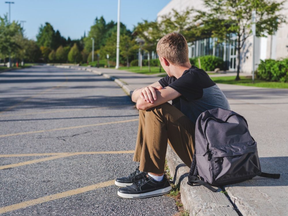 Teenage boy sits on sidewalk