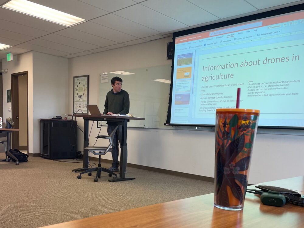 Ram Scholar stands at the front of a classroom and gives a presentation