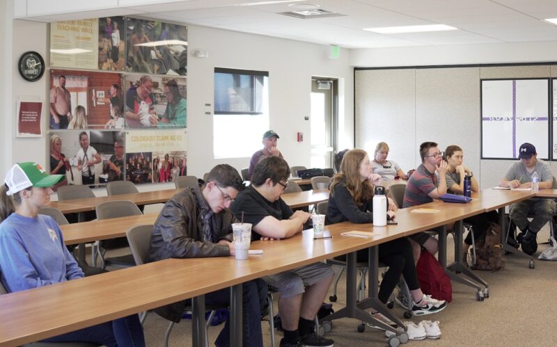Ram Scholars Participants sit at long tables in a classroom. Some write and some listen.