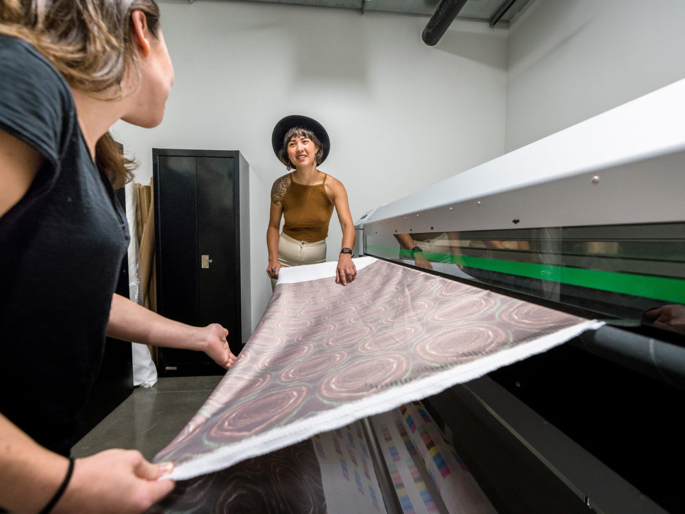 Two students work together to create custom textiles on the fabric printer in the Prototype Lab