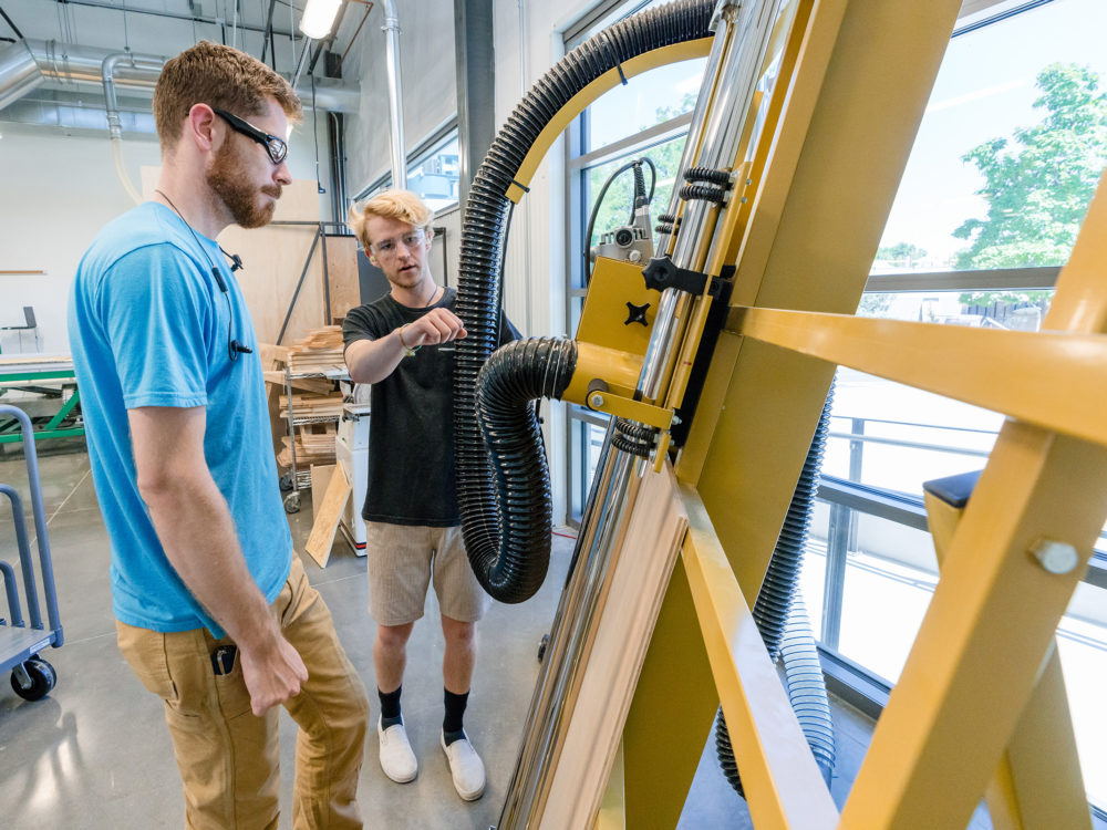An instructor teaches a student how to use the panel saw in the Wood Lab