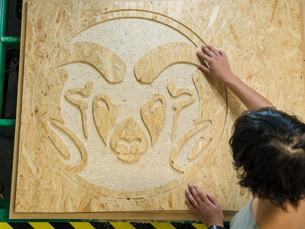 A student checking a logo carved into wood using the CNC router in the Wood Lab