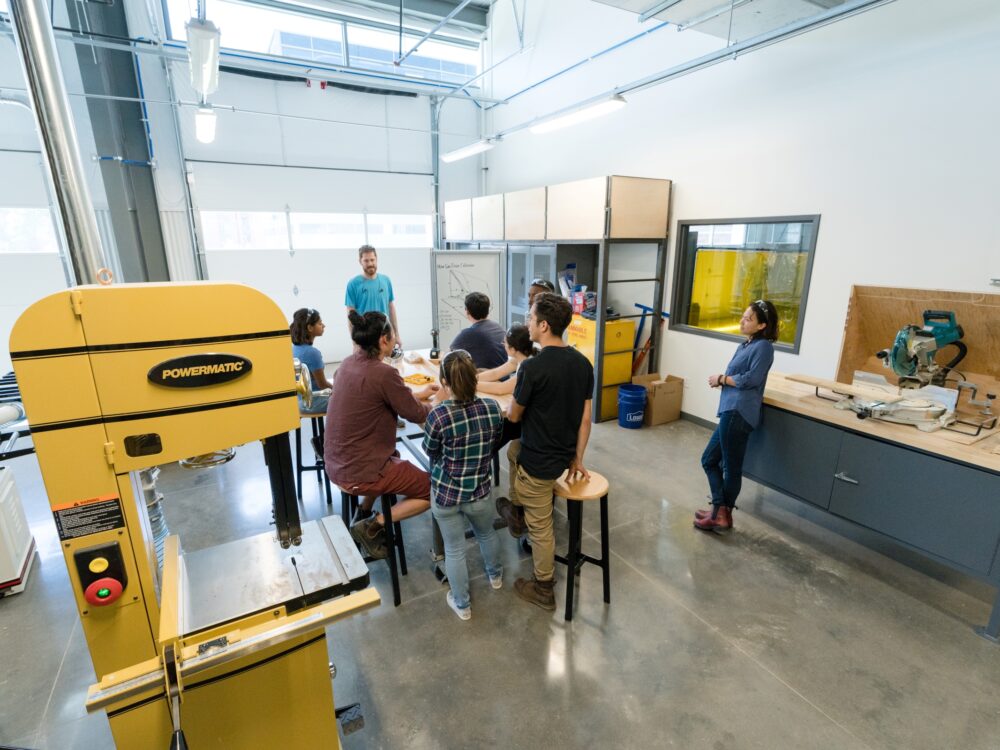 Students and instructors discuss a project at a table in the Wood Lab