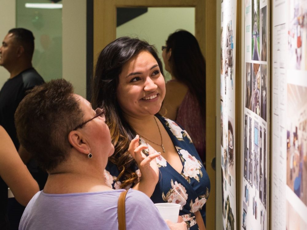 A close-up image of two students looking at a wall of completed design projects during an exhibition at the Nancy Richardson Design Center