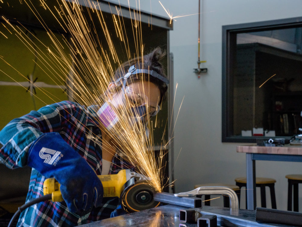 A student creates sparks when using the angle grinder in the Metals Lab
