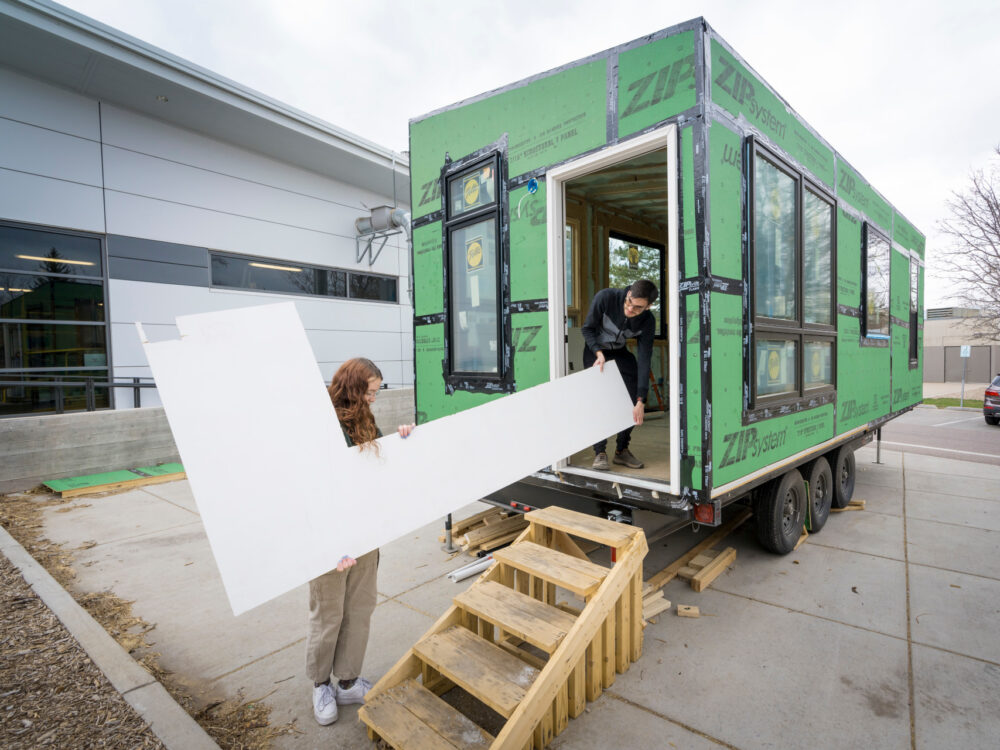 Sesign thinking students carry a large piece of drywall into the 2023 CSU Tiny Home