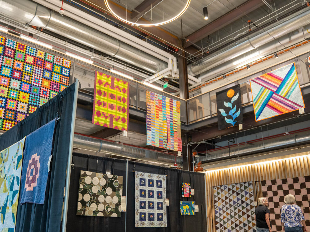 Quilts from the 2023 Fort Collins Modern Quilt Fest are hung from the second story of the RDC Design Exchange