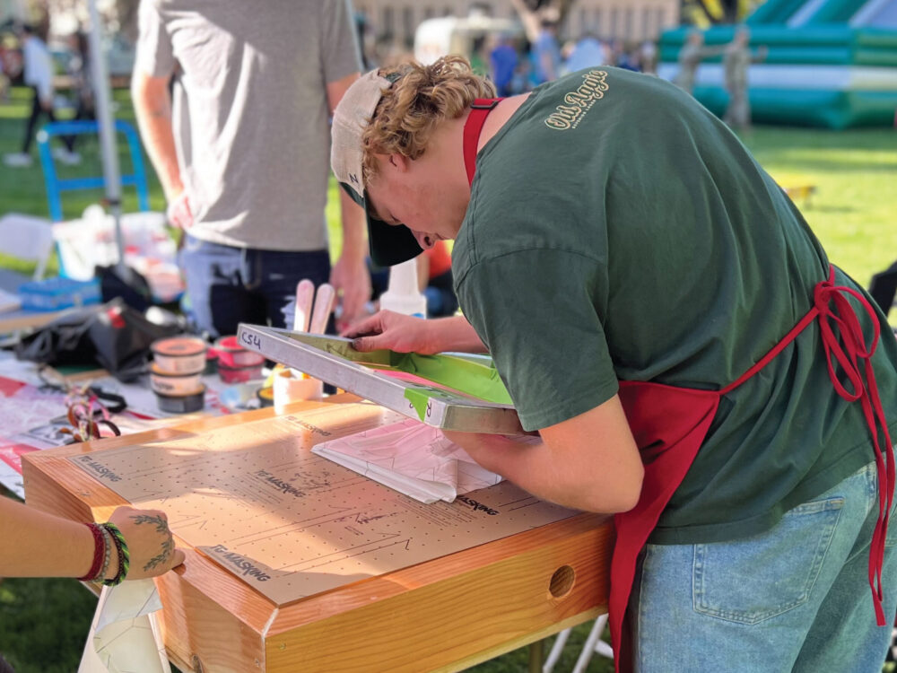 A student fabrication lab monitor demonstrates screen printing during Colorado State University's Homecoming Weekend