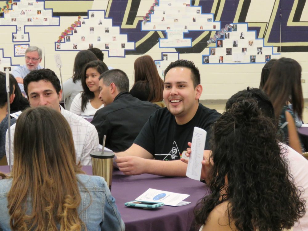 A group of people sit around a table in the Fort Collins High School gym during a Caminos event