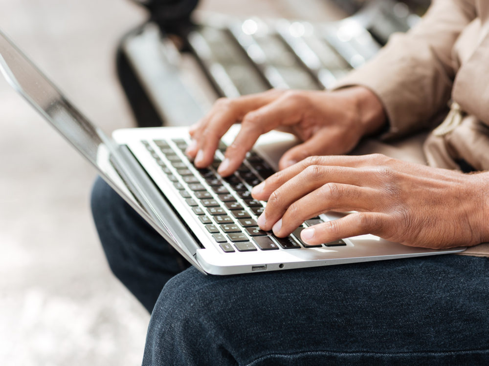 Man with laptop sitting on bench and typing