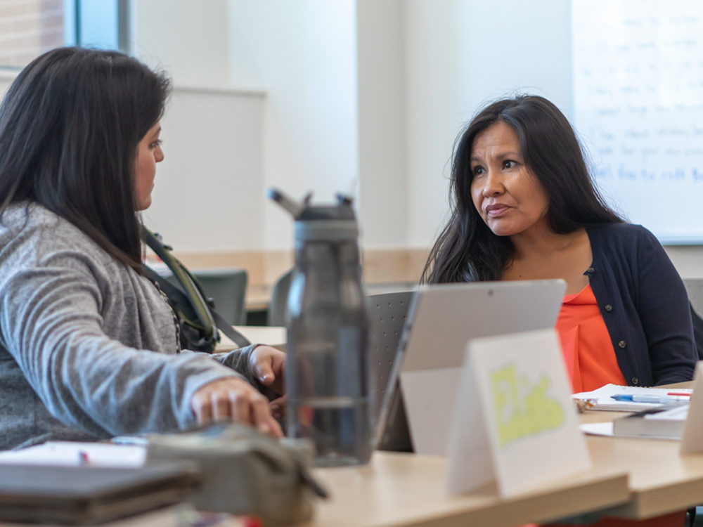 Two Higher Education Leadership students, both presenting as female, sit face-to-face in discussion