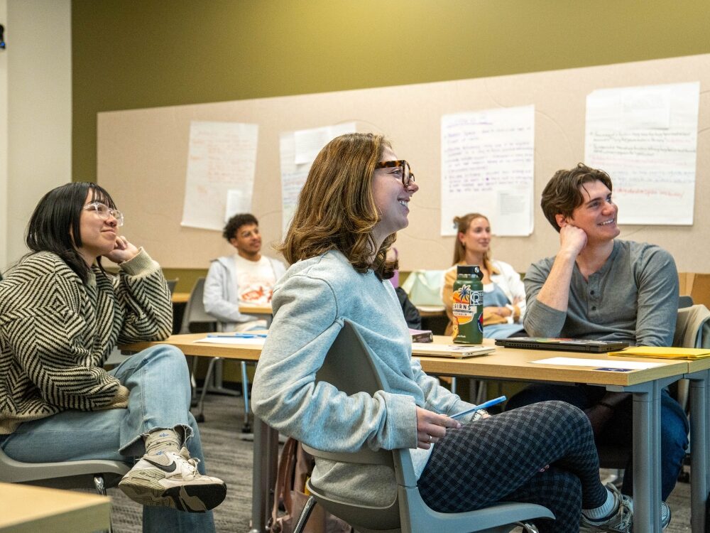 A group of students smile while engaging in conversation in a classroom.