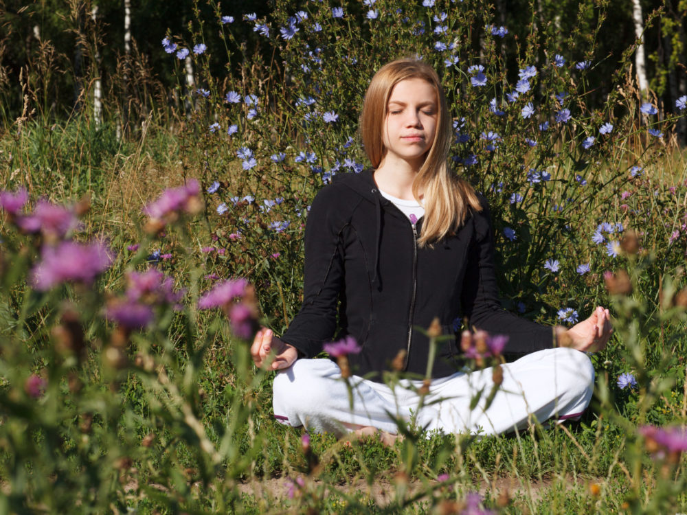 Lotus yoga pose. Woman meditating in the city park at summer morning. Beautiful blue flowers in foreground.