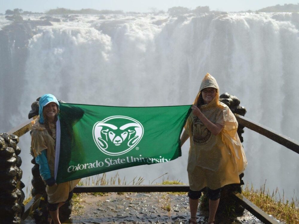 CSU studnets hold up a CSU flag in front of a waterfall in Zambia