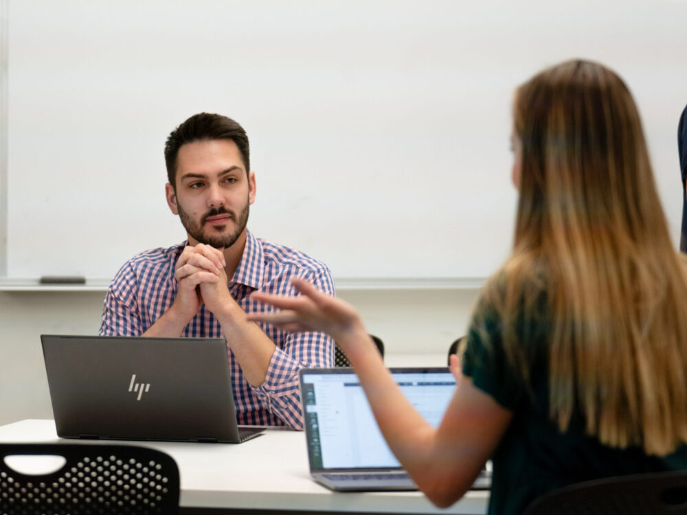 A student smiles as he listens to another student in a small group conversation.