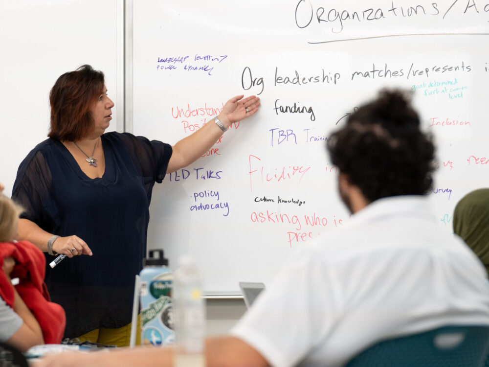 Instrcutor Marie Villescas Zamzow points to a whiteboard as she addresses the class.