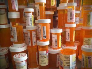A large stack of prescription pill bottles with a person's eye peering through.