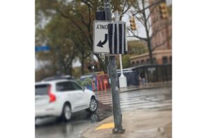 A photo of a rainy road with an upside down street sign.
