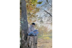A young woman reads a book at the base of a tree on a sunny autumn day