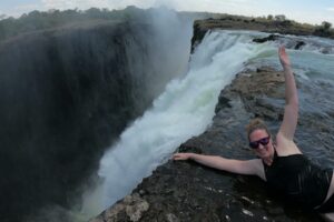 A woman smiles near the cliff of a waterfall on a summer day
