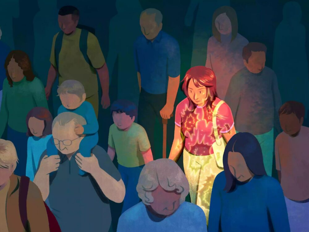 A young person walks through a crowd of people of all ages, under a spotlight. This image is from the article `Why Is Cancer Rising in Young Adults?` on Verywellhealth.com.
