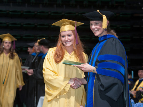 April Mason smiles with a graduating student in commencement regalia.