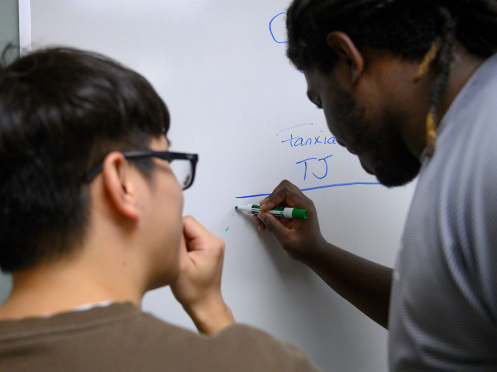 Two people writing on a white board