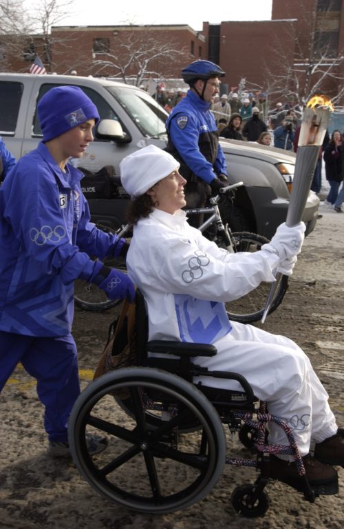 Kelly carrying the Olympic torch being pushed in her wheelchair