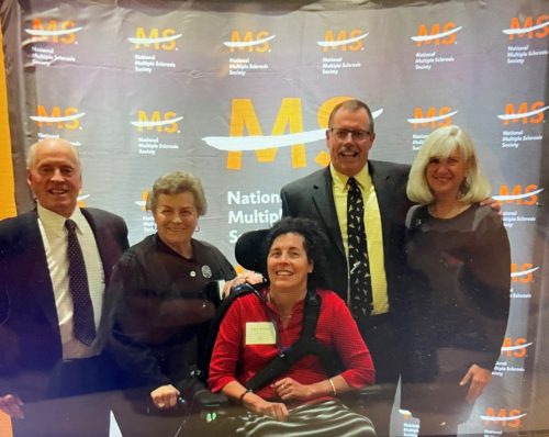 Kelly, her brother and his wife, and her parents in front of an MS background
