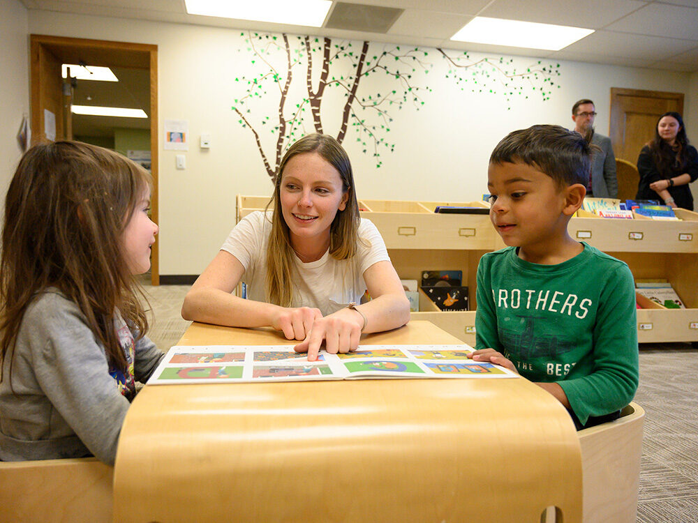 A teacher reads a book with two students in the Early Childhood Center Library