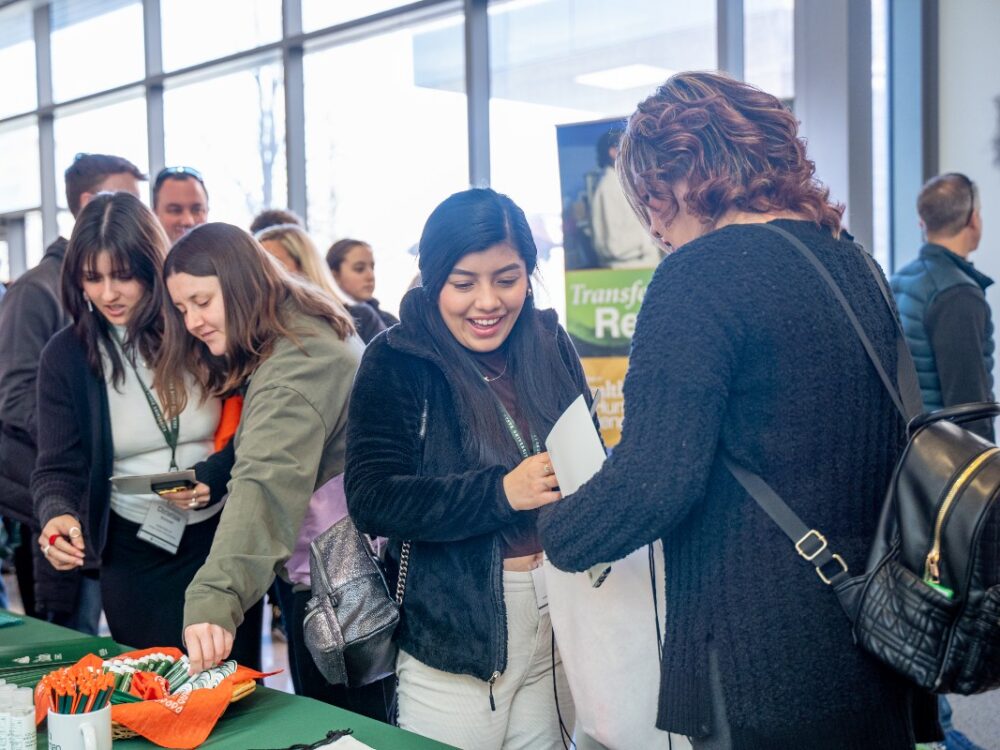 Prospective college students visit a College of Health and Human Sciences table at an event and gather giveaways