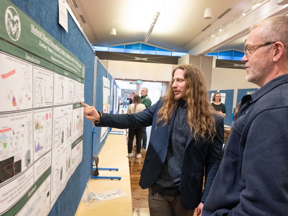 A student points to his research poster while a judge looks on
