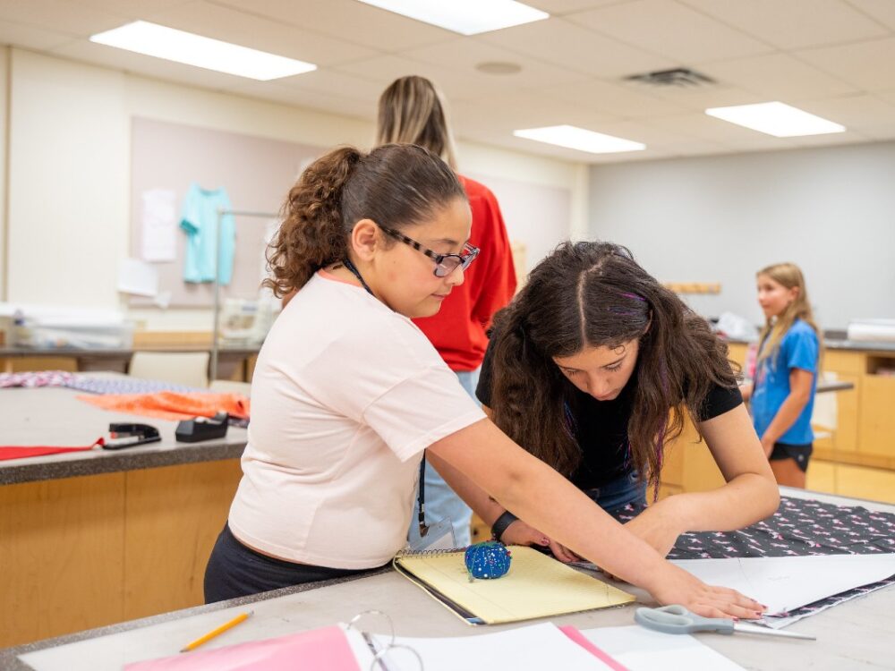 Two girls cut fabric in the sewing lab