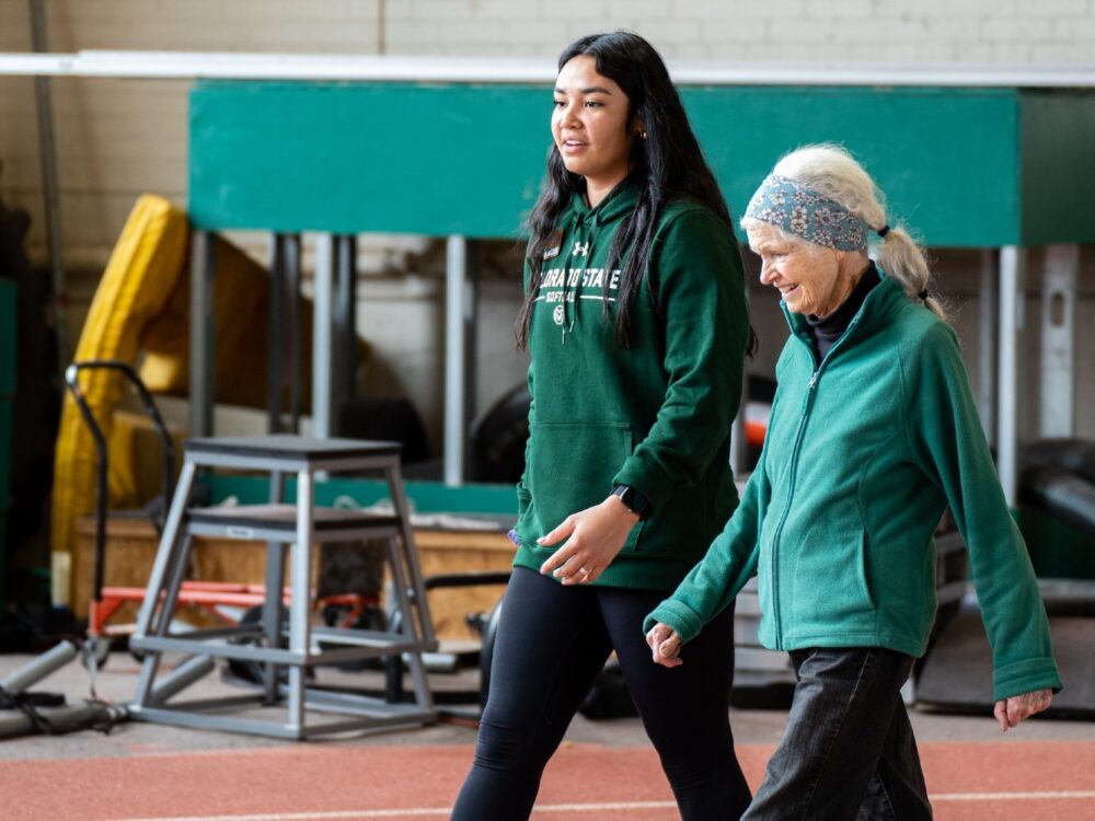 A student walks on an indoor track with an older adult