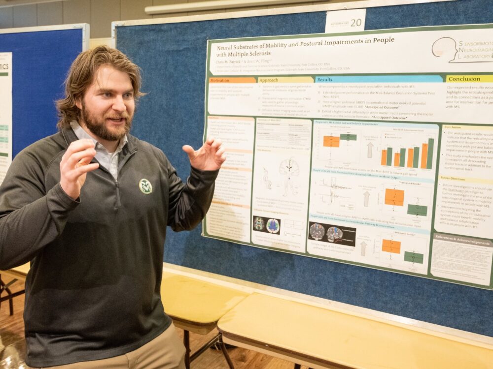 A student stands in front of his research day poster