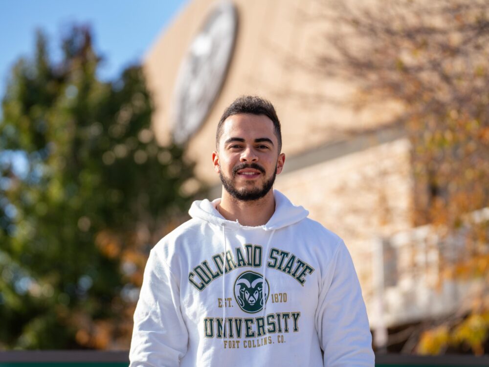 A student wearing a white sweatshirt standing outdoors in front of Moby Arena