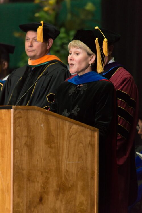 Jodie Hanzlik wearing a cap and gown speaking at a podium